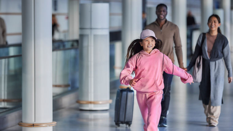 A happy girl running at the airport with her parents and an autowalk at the background – KONE autowalk, KONE escalator.
